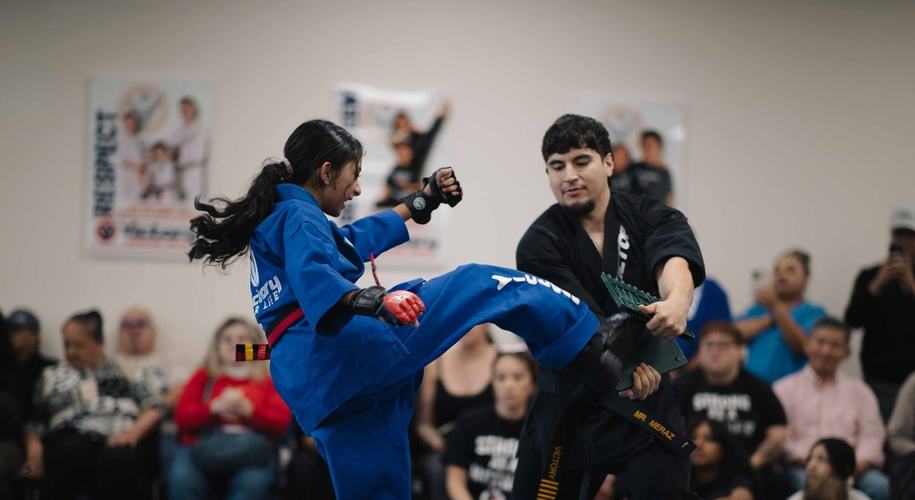 A girl in a blue uniform kicks through a board
