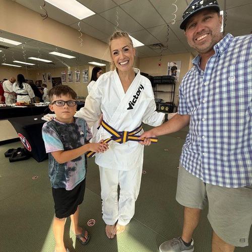 A boy getting his new belt with his mentor and his dad