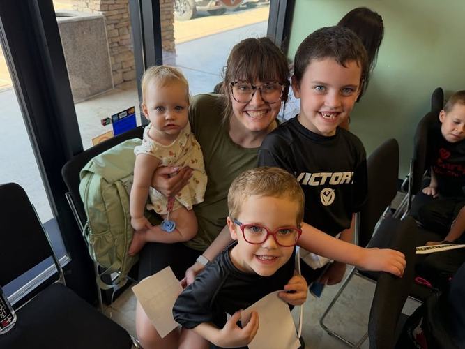 A mom with her baby and two smiling boys holding their boards