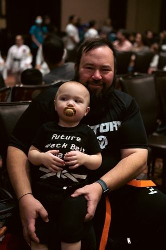 A dad holds his baby in a Future Black Belt shirt