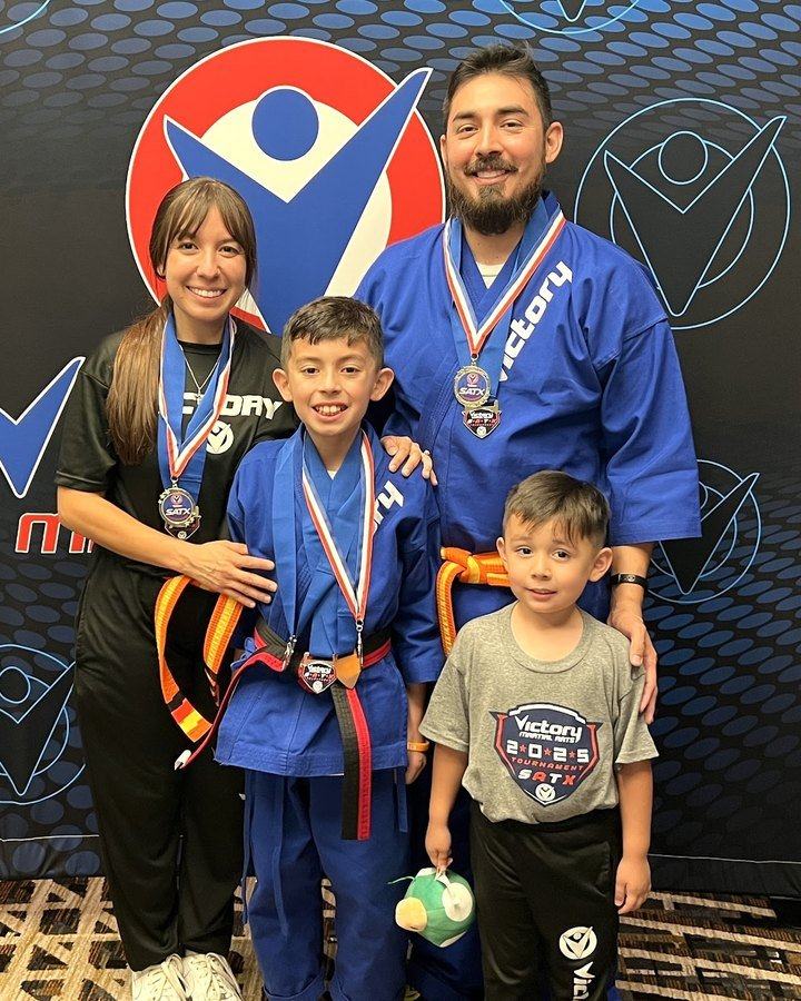 A grinning boy with his medal stands with his mom, dad and little brother in front of a Victory backdrop