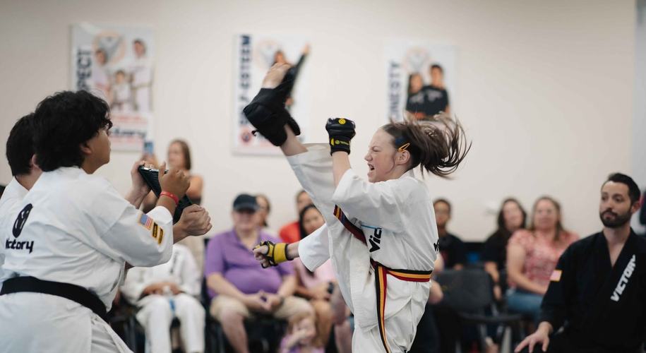 A girl lands a high kick on a pad
