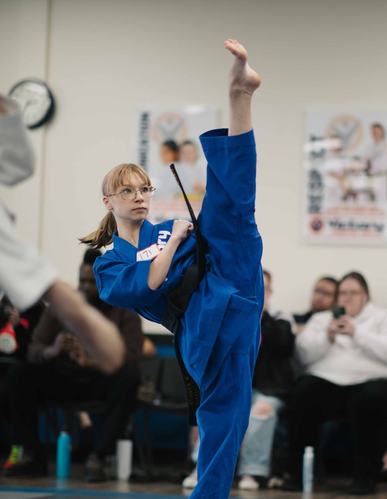 A girl in a blue uniform holds a vertical kick
