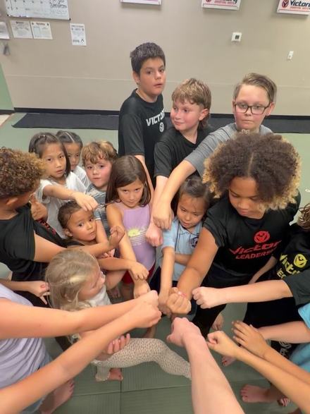 Kids and instructors join fists in a circle on the mat