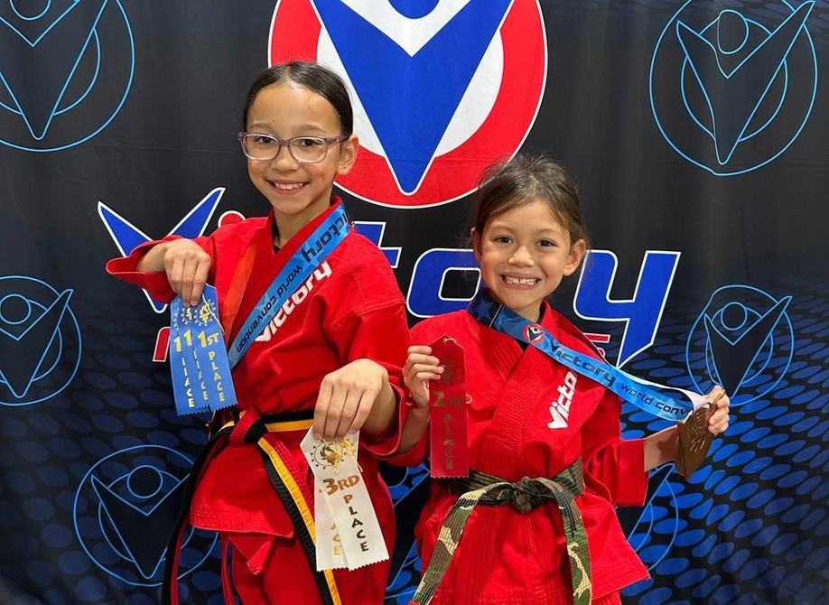 Two sisters in red uniforms smile with their medals