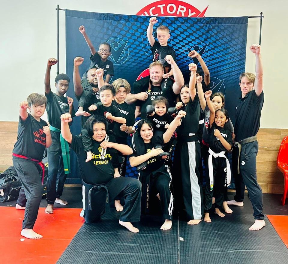 A Victory class of kids and their mentors, fists raised in front of the Victory backdrop