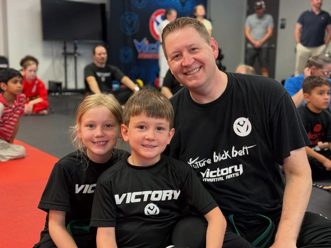 A dad sits on the mat with his son and daughter