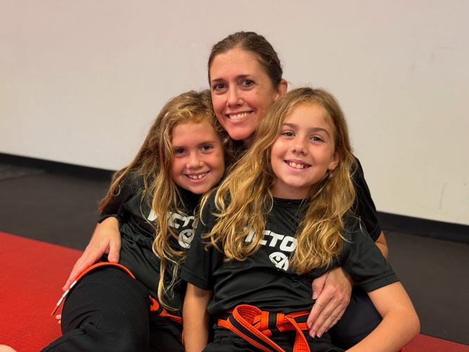 A mom hugs her two daughters on the mat